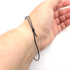 Black cord bracelet with adjusting knots around a wrist