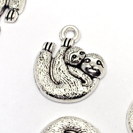 silver jewelry charms that look like mom and baby sloth hanging on a branch