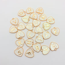 white and light gold heart shaped jewelry charm with letters on them