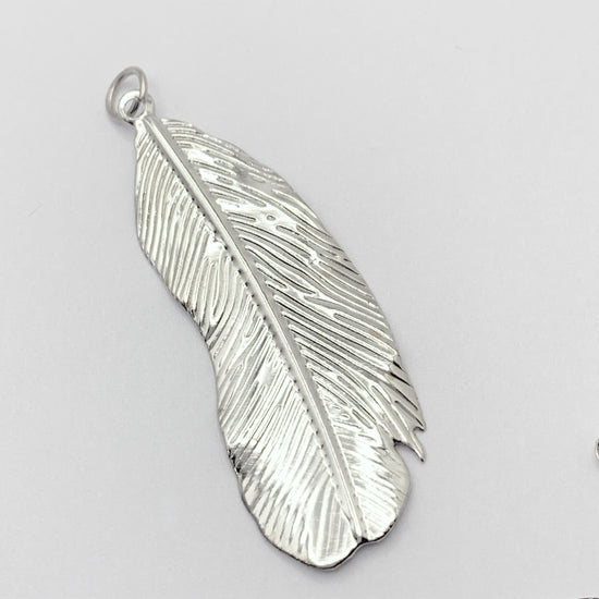 silver colour jewelry pendant that looks like a feather
