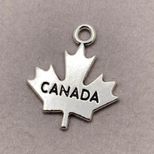silver jewerly charm in the shape of a maple leaf with canada engraved on it