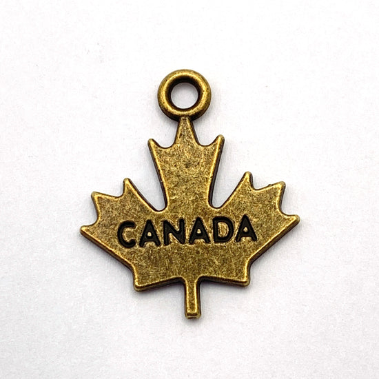 Bronze jewerly charm in the shape of a maple leaf with canada engraved on it
