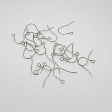 A pile of silver-colored earring hooks for jewelry making, scattered on a plain light gray background.
