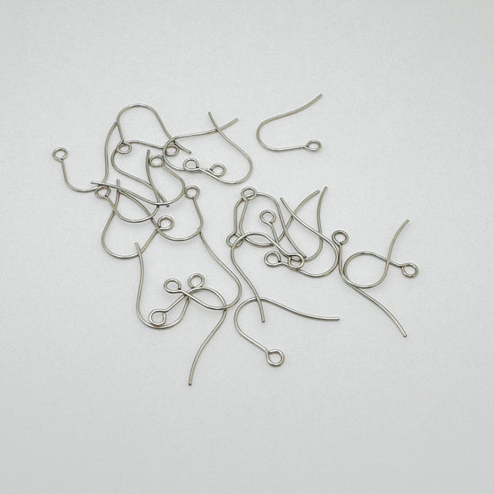 A pile of silver-colored earring hooks for jewelry making, scattered on a plain light gray background.