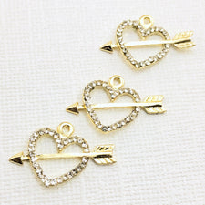 3 jewelry charms that are gold color shaped like a heart with an arrow through it