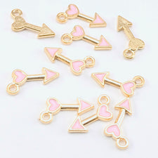 arrow shaped jewerly charms that are gold with pink enamel