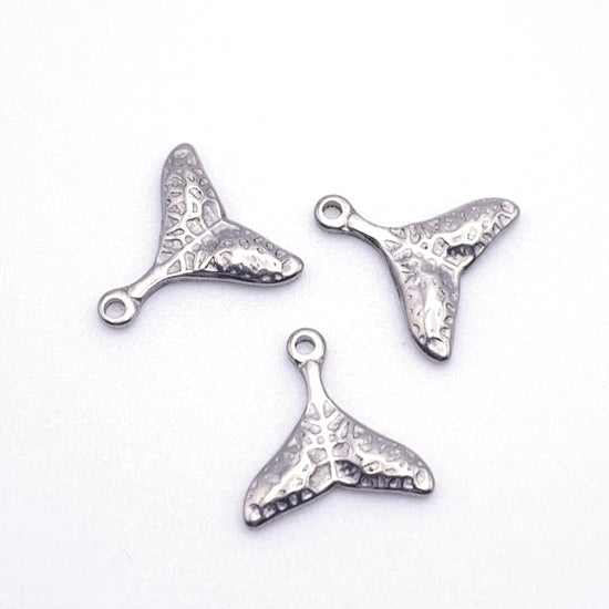 three silver jewelry charms shaped like a whale tail