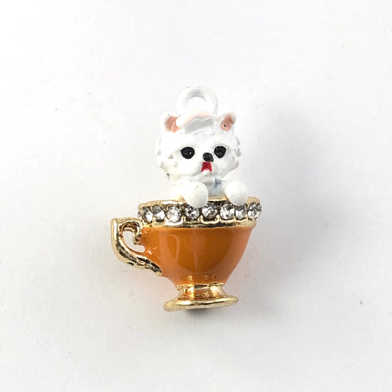 Jewelry charms that look like a white dog in an orange teacup with rhinestones around the rim of the cup